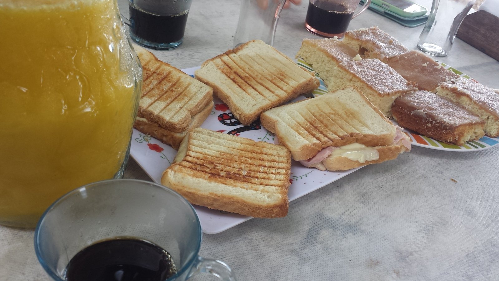 Café da Manhã com bolos, misto quente, jarra de café e de suco natural de manga